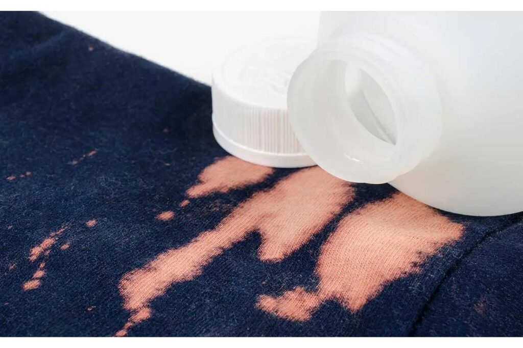 Bottiglia di candeggina accanto a vestiti scoloriti, evidenziando i rischi per i tessuti delicati.