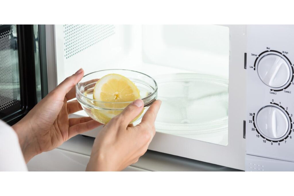Persona pulisce microonde con panno umido, vapore visibile, cucina ordinata e sicura sullo sfondo.